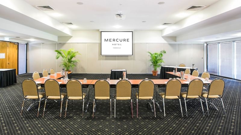 U-shape setup in Burdekin Room with a projector screen, tables and chairs at Mercure Hotel Townsville