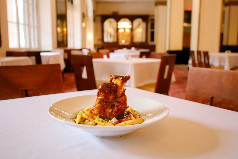 Braised meat over pasta in a white bowl on a dining table surrounded by chairs at Arlington Resort Hotel & Spa