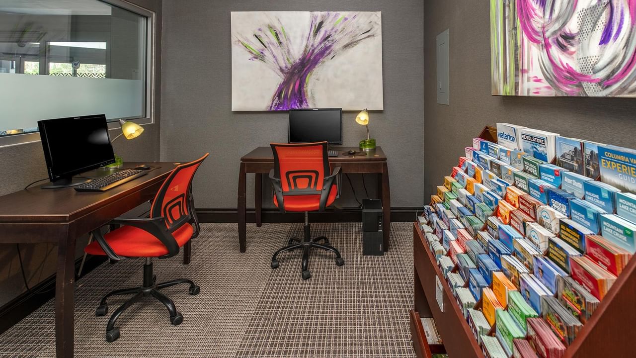 Business center with computer workstations, orange chairs, and colorful brochure display at Coast Calgary University Area Hotel by APA