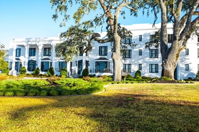The white, columned The White House Hotel building viewed from a large, grassy lawn on a lovely sunny day