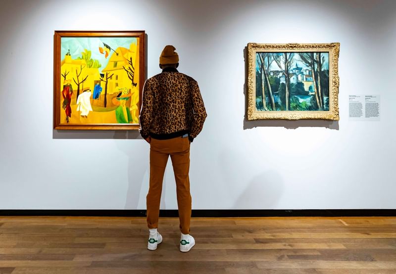 Person in leopard print jacket viewing two framed paintings on white gallery wall at Warwick Le Crystal Montreal