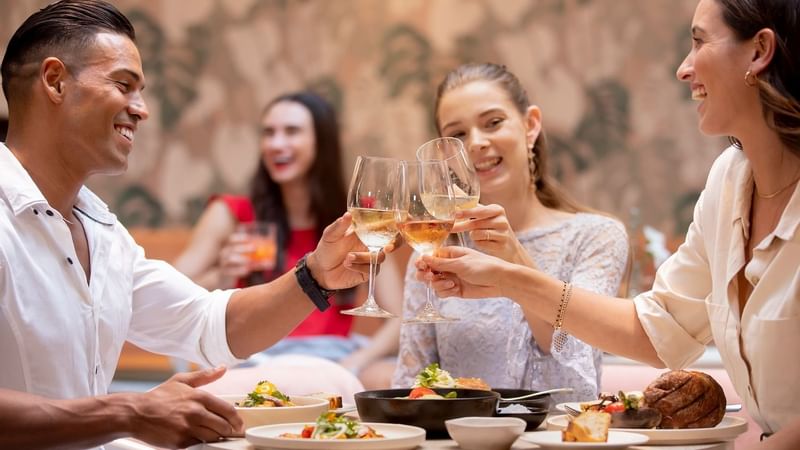 Friends toasting wine at an outdoor table in The Marke Kitchen at Novotel Sydney International Airport