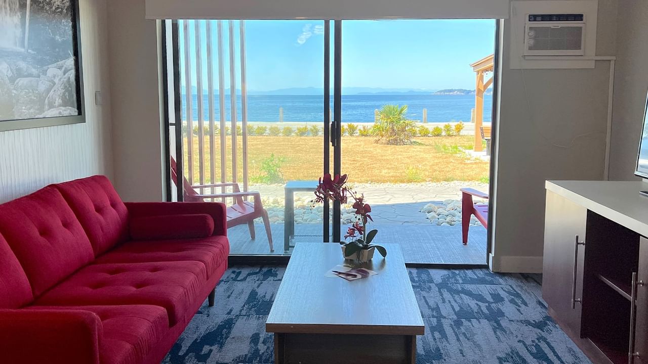 Guest room living area with red couch, coffee table, tv, patio doors, ocean view and patio with red deck chairs