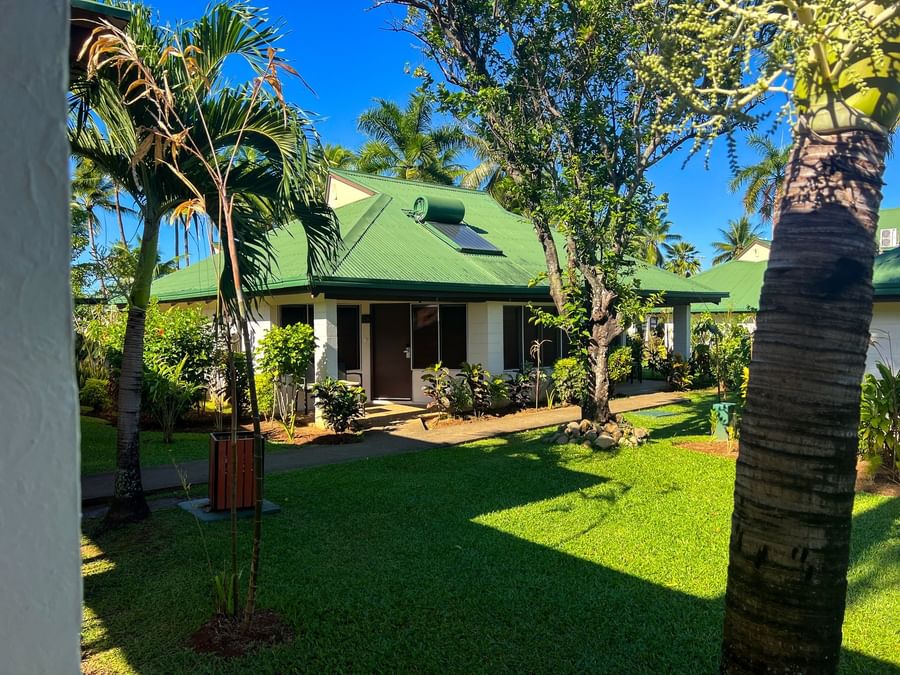 Green-roofed bungalows by palm trees and lush lawns under a clear blue sky at TokaToka Resort Nadi Fiji