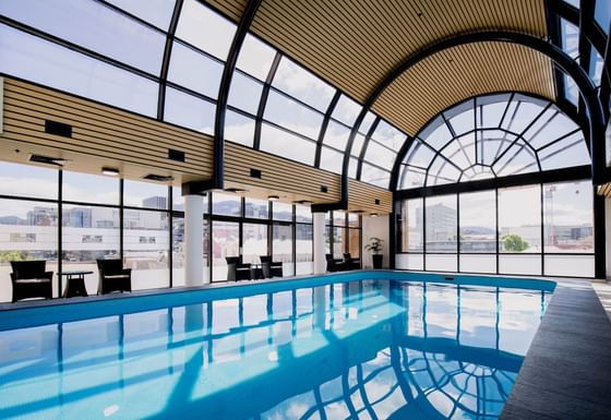 An indoor pool with arm chairs and view of the city at Hotel Grand Chancellor Hobart