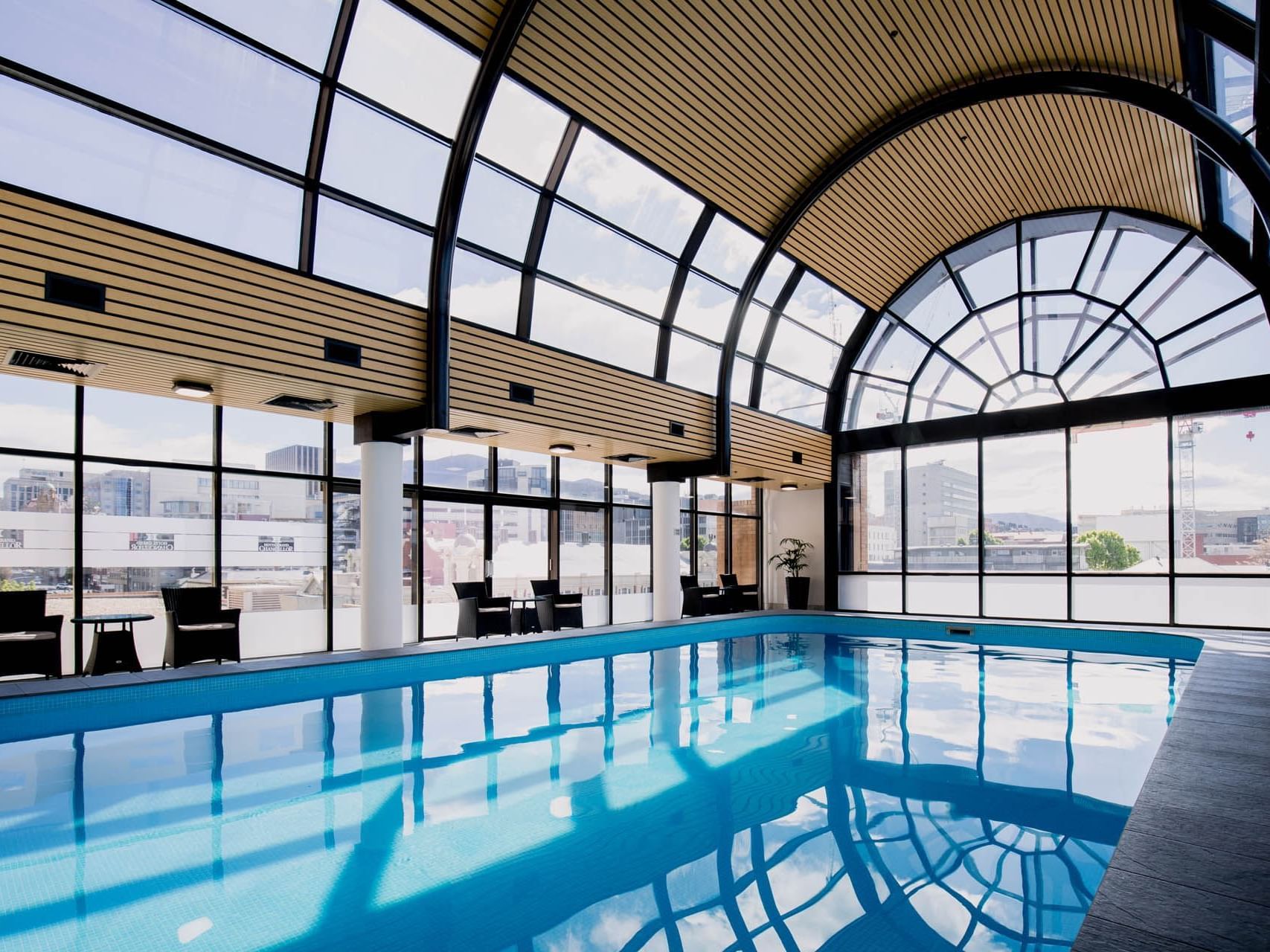 An indoor pool with arm chairs & city view at Grand Chancellor Hobart