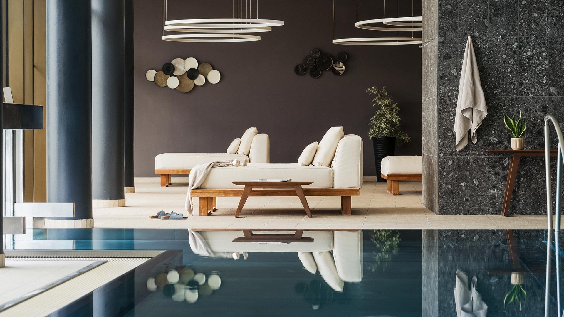 Piscina coperta con lettini e piante, riflessa in acqua, e decorazioni moderne.
