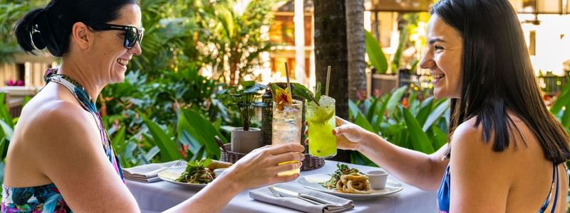 Two women enjoying cocktails and lunch together at an outdoor restaurant at Pullman Palm Cove Sea Temple Resort & Spa
