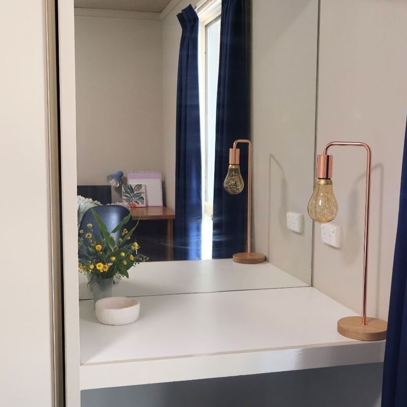 Mirror reflecting a room with blue curtains and a vase of flowers at La Trobe University Villas.