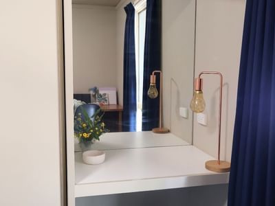 Mirror reflecting a room with blue curtains and a vase of flowers at La Trobe University Villas.