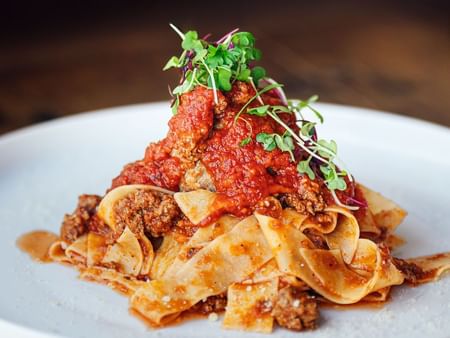 Pasta dish with sauce and herbs on a white plate on a wooden surface at Warwick Hotels and Resorts