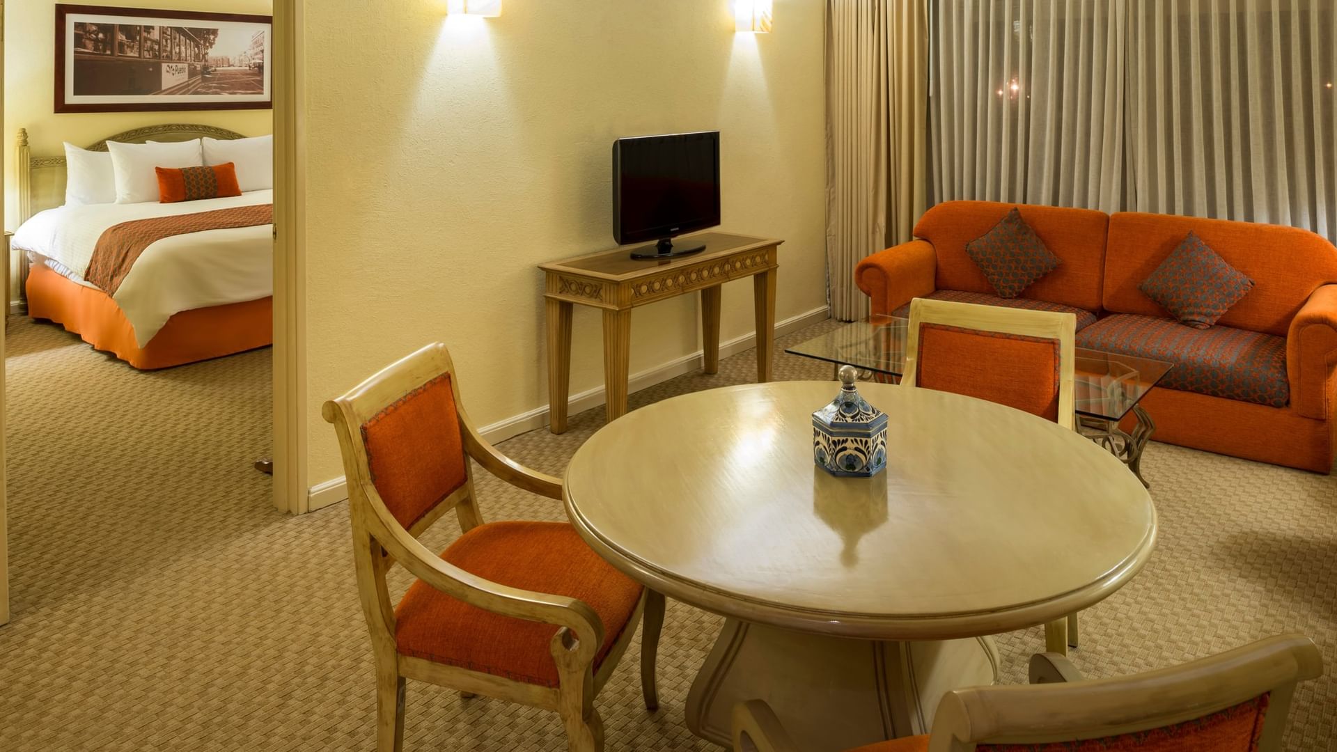 Master Suite King con sala de estar, sofá naranja y dormitorio al fondo en Camino Real Puebla Angelópolis