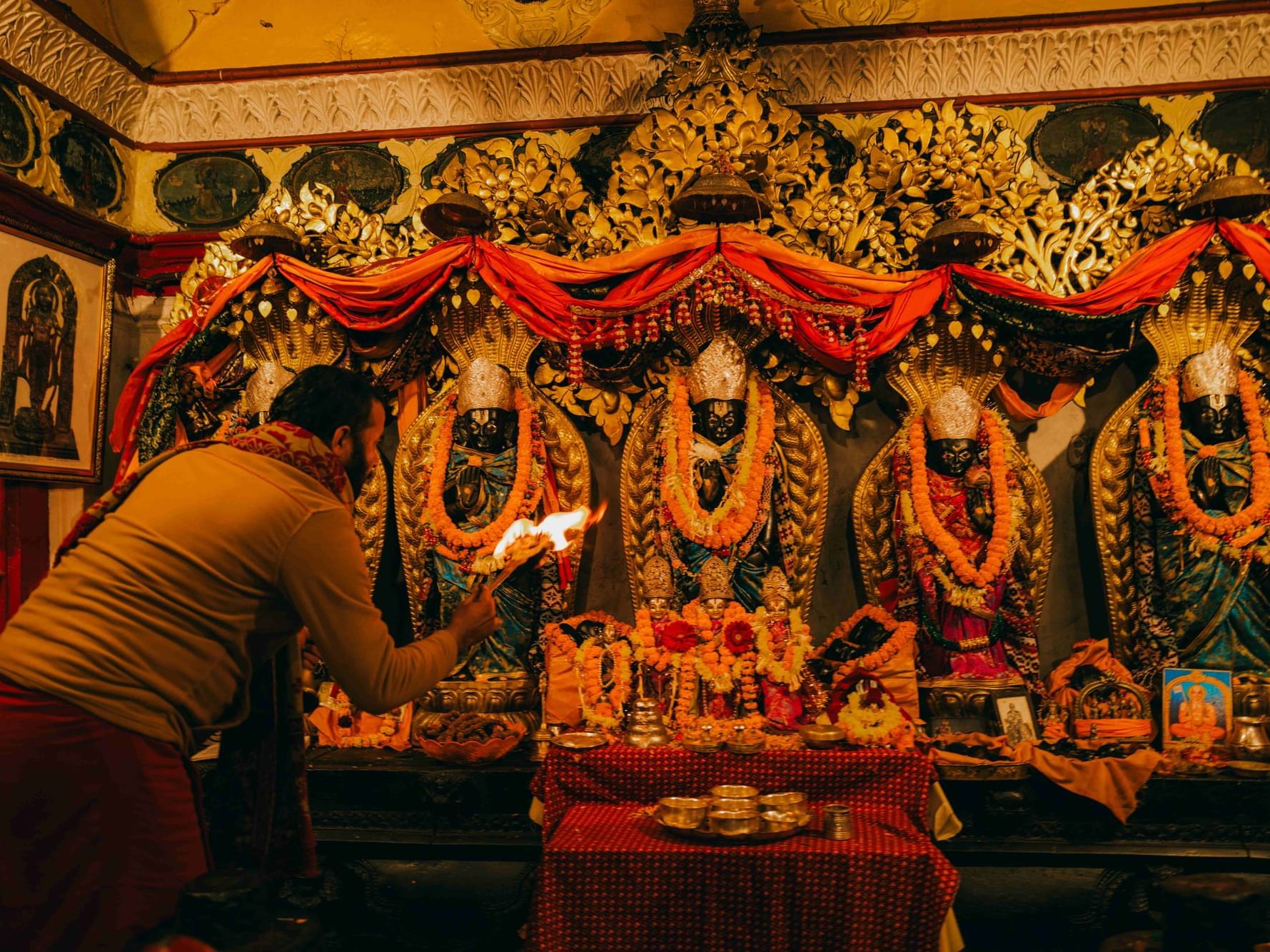 Man performing a ritual in front of ornate Hindu deities adorned with flowers near Dwarika's Hotel Kathmandu