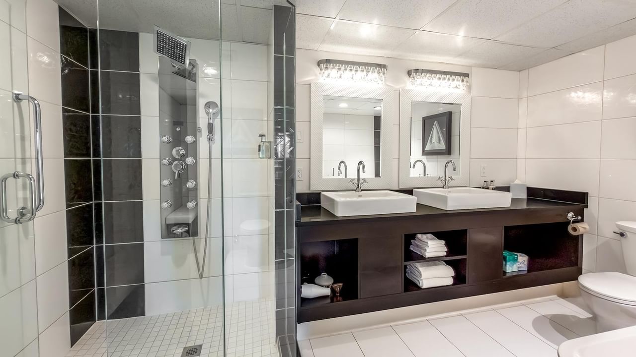 Modern bathroom with dual vessel sinks, walk-in shower, and dark wood vanity at Coast Calgary University Area Hotel by APA