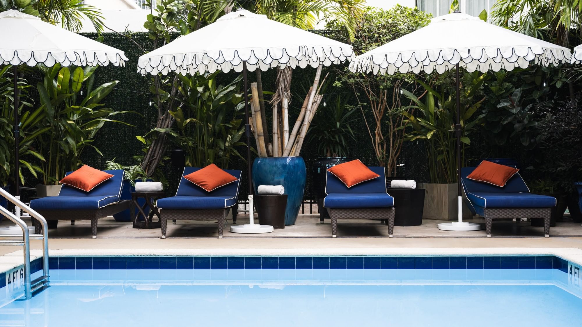 A poolside scene with lounge chairs, umbrellas, and tropical plants.