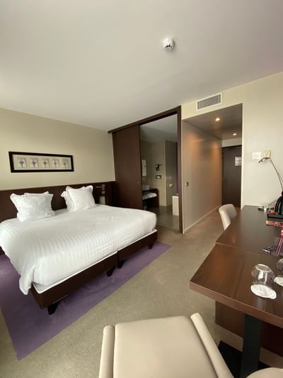 Chambre d'hôtel avec lit, bureau, chaises, et salle de bain visible dans l'ouverture.