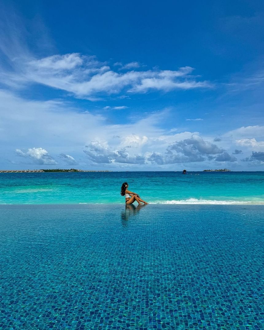 Lady sitting on the edge of an infinity pool overlooking the sea and blue sky near Park Hotel Group