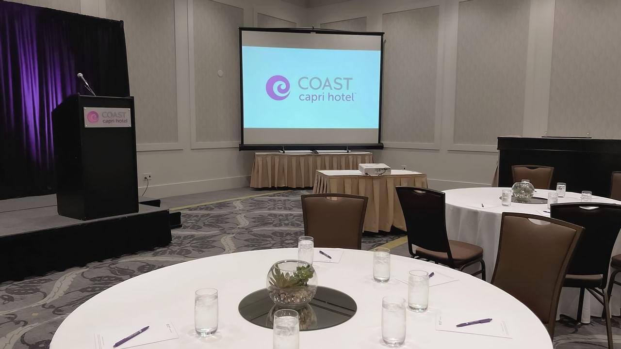 Ballroom with round tables, chairs, stage, podium and presentation screen