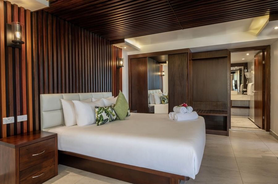 King bed by a dark wood-slat wall under a ceiling with rolled towels in Warwick Suites at Warwick Fiji Resort and Spa