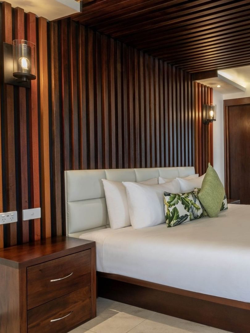 King bed by a dark wood-slat wall under a ceiling with rolled towels in Warwick Suites at Warwick Fiji Resort and Spa