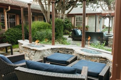 Outdoor patio with wicker furniture, stone fire pits, and a view of a house and garden.