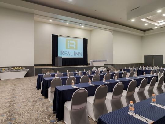 Nápoles meeting room with classroom set-up, bottled water, and a large projector screen at Real Inn Tijuana