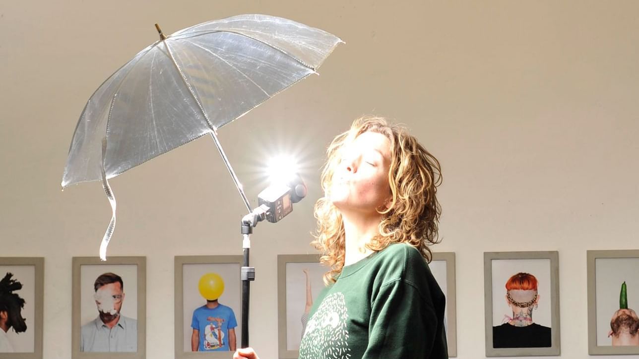 A woman with a flash umbrella stands in her photo studio.