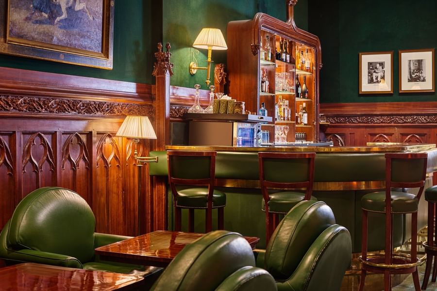 Green leather chairs by a wood-paneled bar with shelves of drinks under soft lights at Hotel Westminster Paris