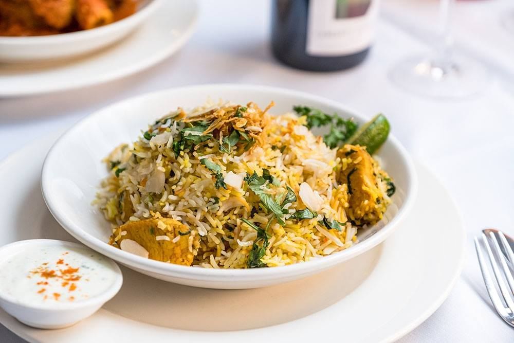 a white bowl of rice and meat on a white table