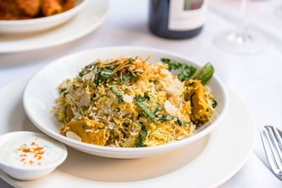 Spice Symphony bowl of rice and meat dish garnished with herbs, with sauce and wine on a table.