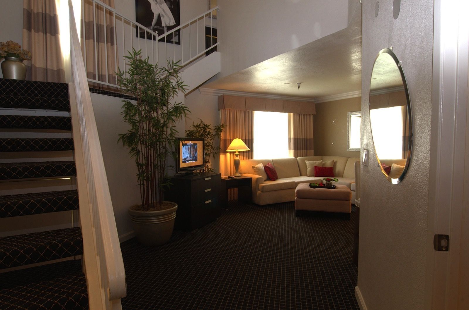 A wide view of a living room with a staircase, sofa, TV, and potted plant.