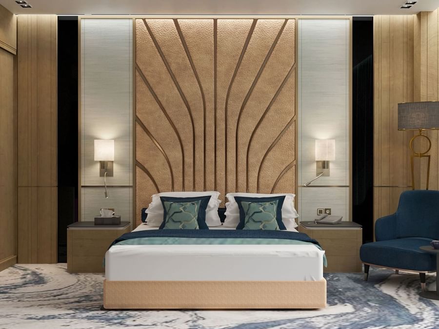 Modern bed with a patterned headboard by a blue chair in the Ambassador Suite at Cantonal Hotel by Warwick Riyadh
