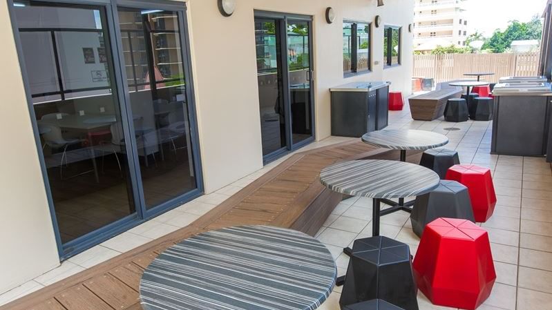 Outdoor terrace with striped round tables, red and black geometric stools, and glass doors at StudentLiving - on Margaret