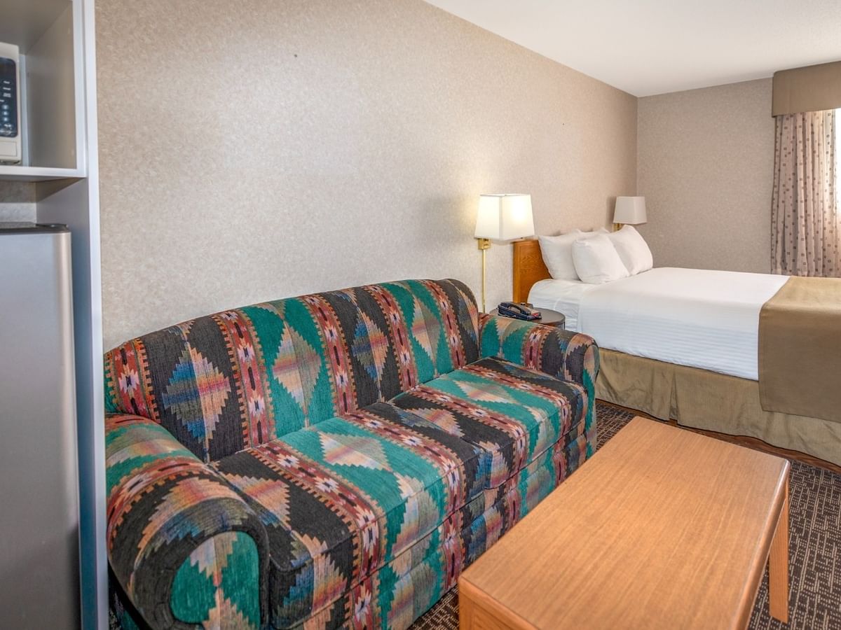 Hotel room with bed, couch, coffee table, and microwave on a shelf.