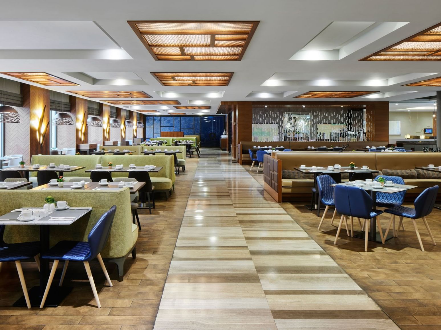 Modernes Restaurant mit Holzboden, heller Beleuchtung und Sitzmöbeln in Blau und Grün – Titanic Chaussee Berlin.
