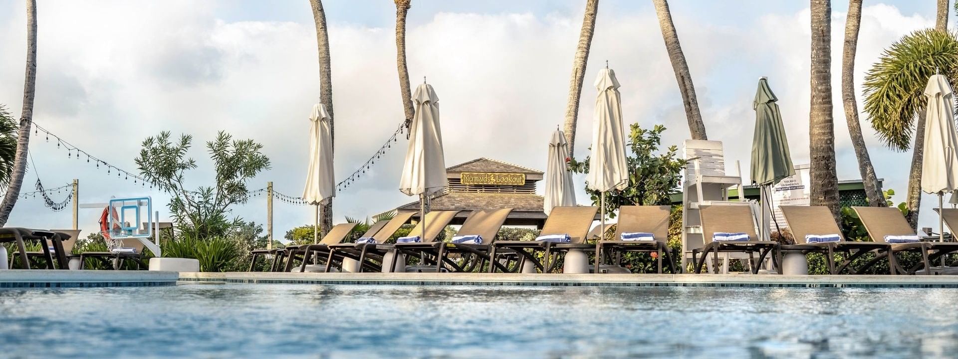 White umbrellas by lounge chairs under tall palm trees surrounding a serene pool at Warwick Paradise Island Bahamas