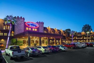 Evening view of the illuminated castle-style entrance with stone towers and covered porte-cochere at London Bridge Resort