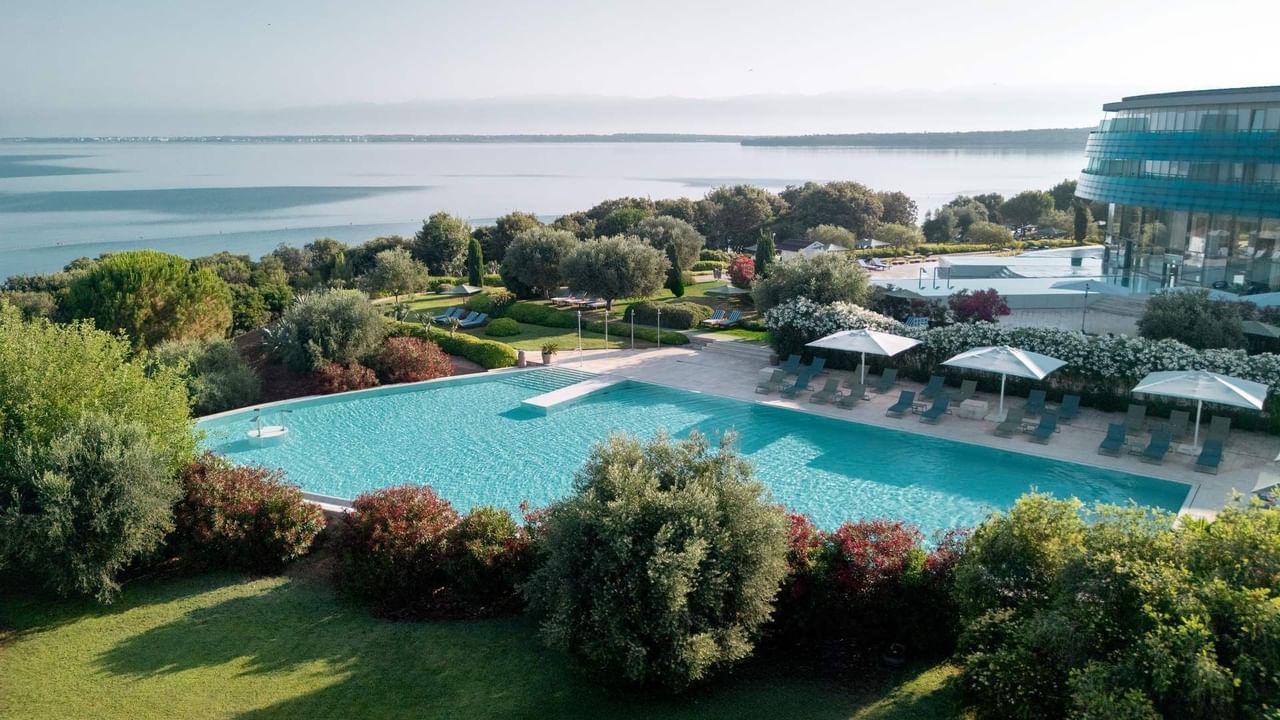 Piscina con ombrelloni e vista sul mare con edifici moderni sullo sfondo.
