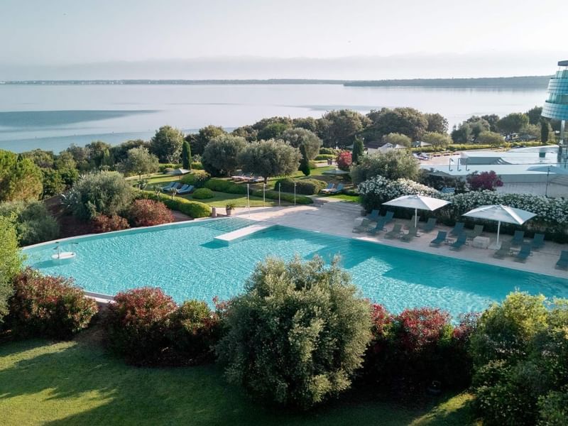 Piscina con ombrelloni e vista sul mare con edifici moderni sullo sfondo.