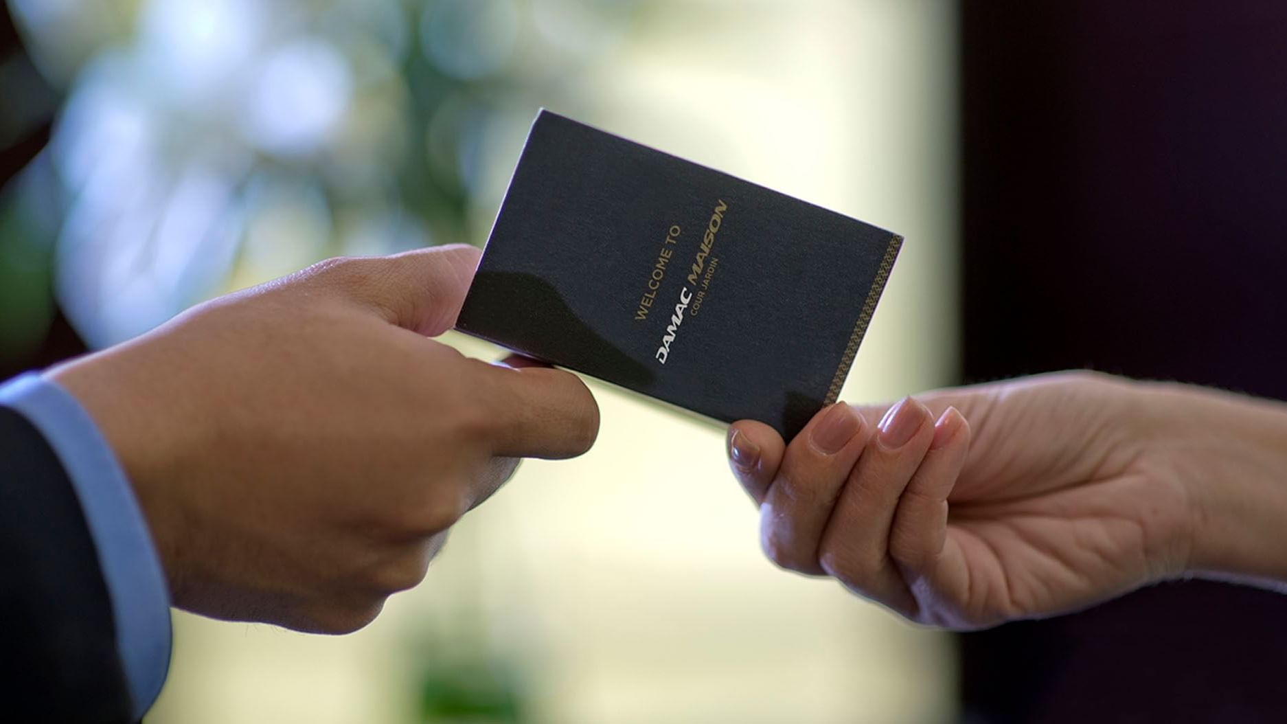 Close-up of a person passing a passport to another person at DAMAC Maison Cour Jardin