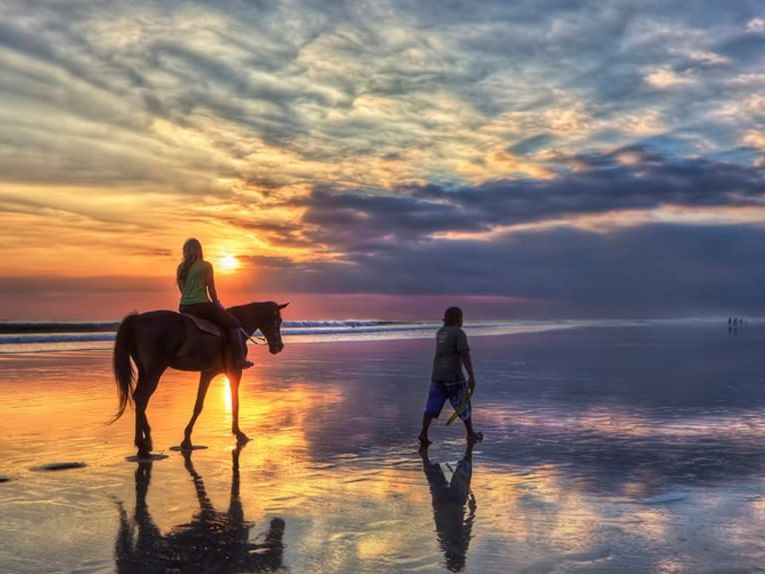 Woman riding a horse on the shore near Eastin Ashta Resort Canggu during sunset