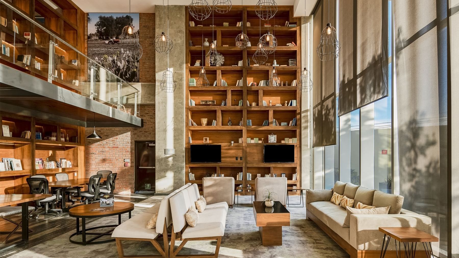 Modern lounge with wooden bookshelves, stylish seating, and pendant lights at Fiesta Inn Suites Aeropuerto del Bajío