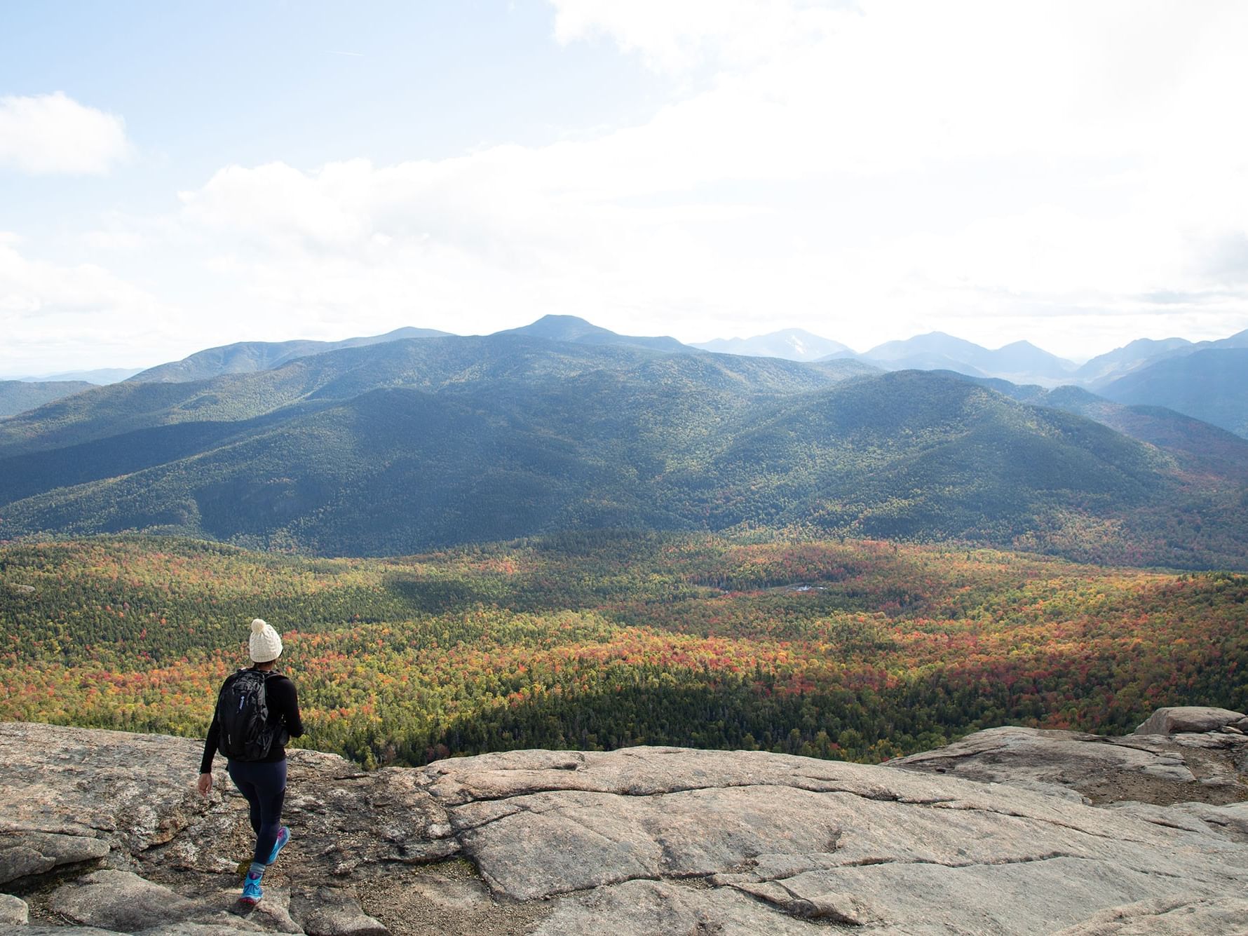 Hiker on rocks overlooking a valley with autumn foliage and distant mountains near High Peaks Resort