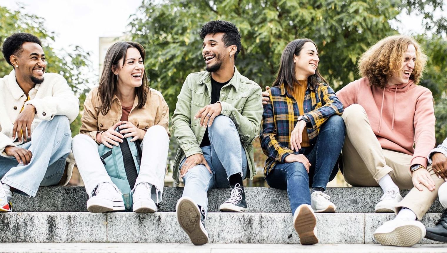 Group of young friends sitting together on outdoor steps and engaging in conversation near UniLodge Canada