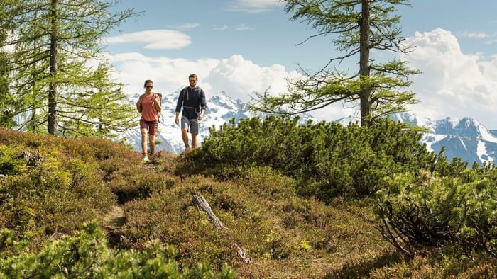 Two hikers with backpacks on a trail and mountains in the background at Falkensteiner Hotel Schladming