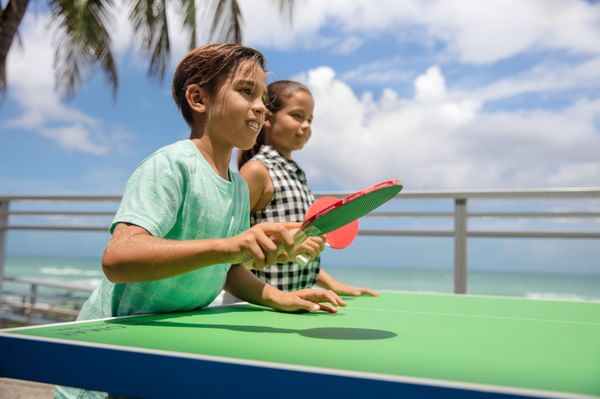 Two children playing ping pong at The Diplomat Resort with the ocean visible in the background