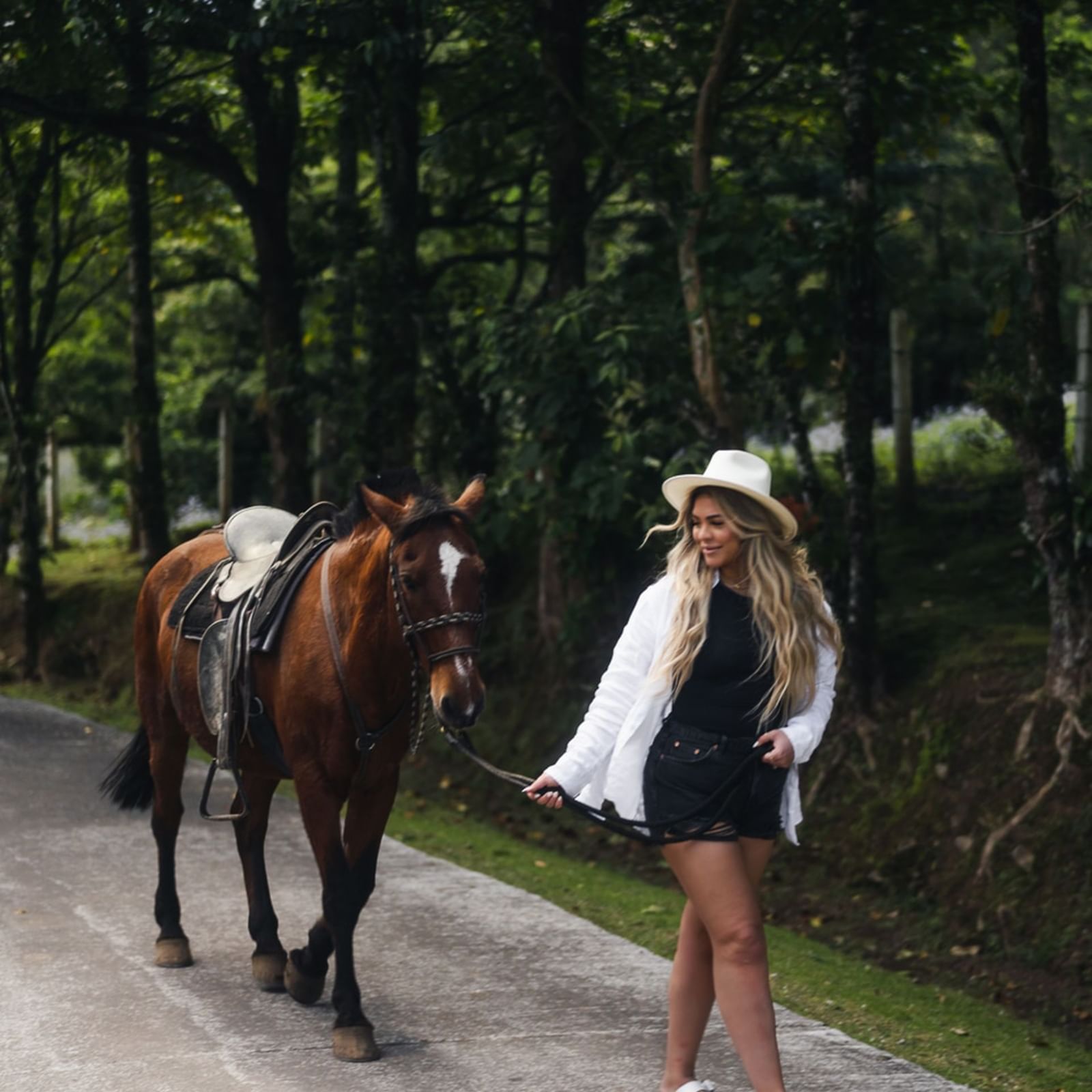 Lady leading a brown horse on a path surrounded by trees at El Silencio Lodge and Spa