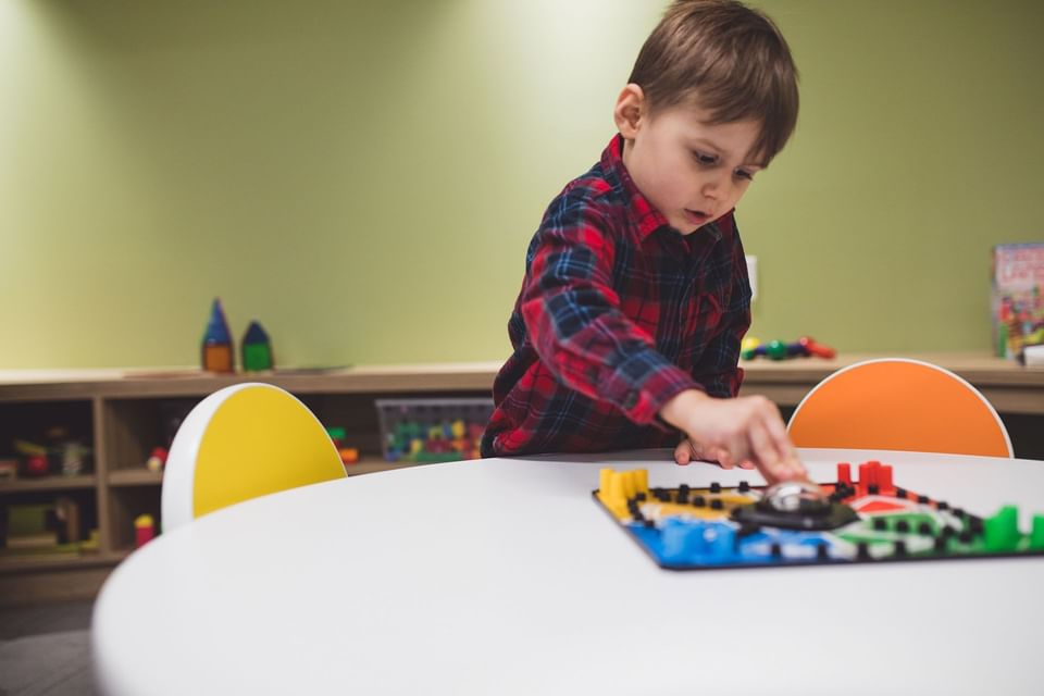 Young boy playing a board game on a round table inside the colorful children play area playroom at Hotel X Toronto