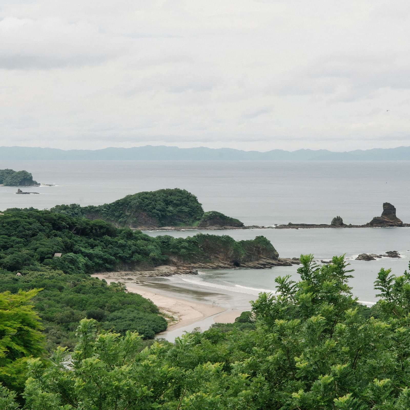 Pristine sandy beach by rocky cliffs and green forest under a cloudy sky near Morgan's Rock Reserve & Ecolodge