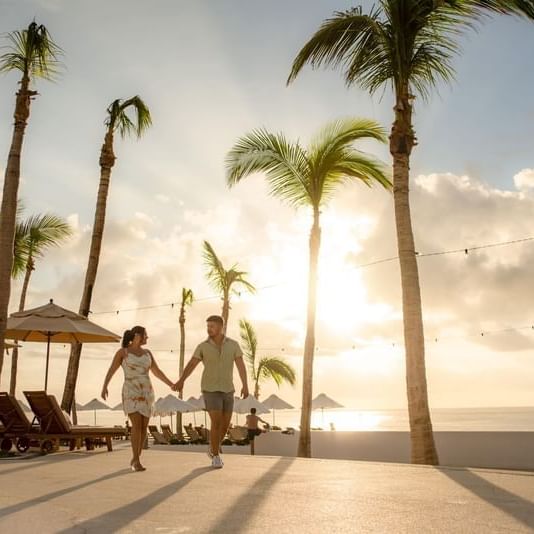 A couple walks hand in hand at sunset under palm trees at Marquis Los Cabos Resort with the ocean in view